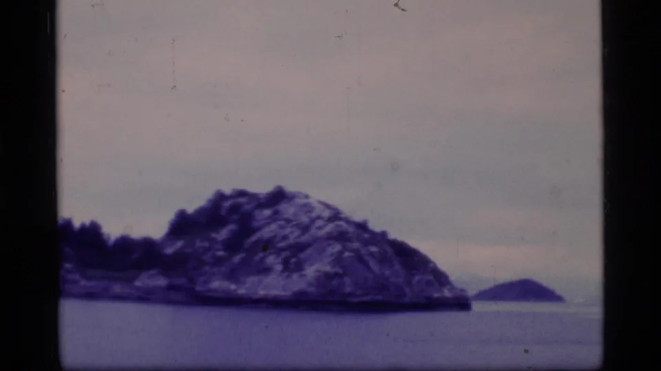 Glacier Bay shoreline with a rocky island and a small distant landform, filmed from the water on 8mm.