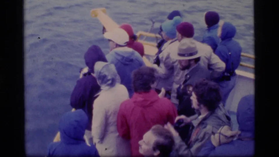 Bundled tourists stand on a sightseeing boat in Glacier Bay, looking out over the water in 1977 home-movie footage.