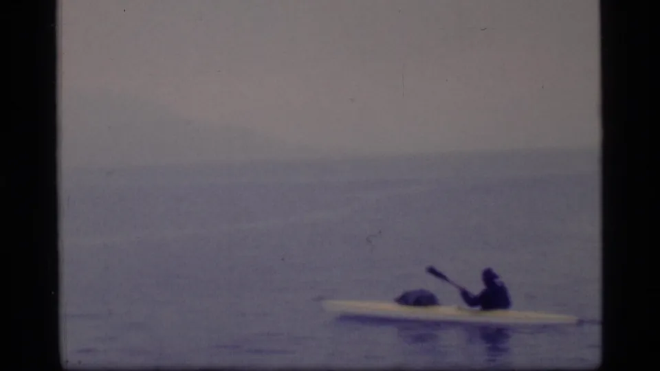 The kayaker appears small against the wide Glacier Bay water and hazy horizon in this 1977 8mm frame.