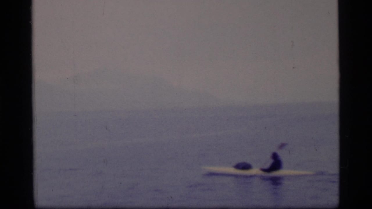 Lone kayaker on calm water with misty mountains in the distance.