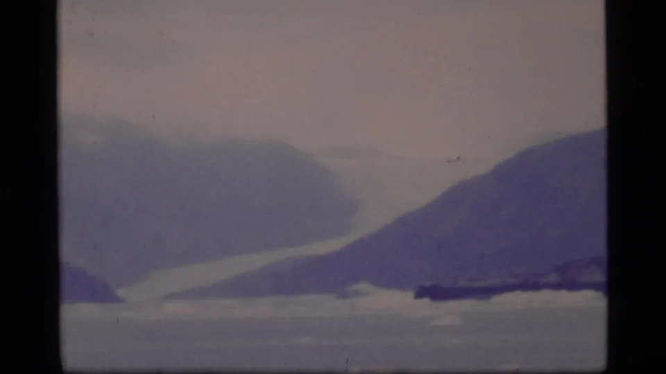 A glacier or snowfield appears between mountain slopes across Glacier Bay, rendered in soft, grainy 8mm film texture.