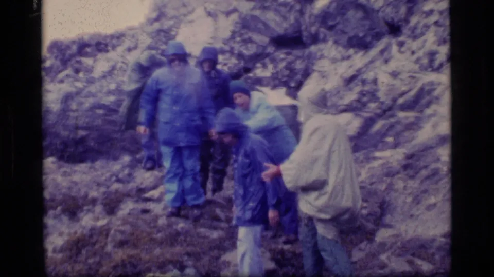 A small group of 1977 Glacier Bay hikers gathers on wet rocks, with one person crouched and others standing nearby.