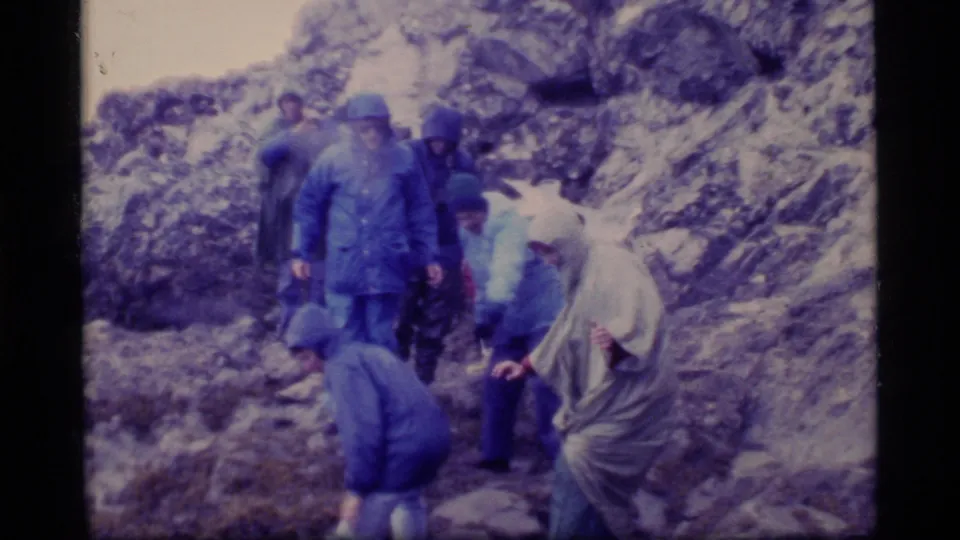 Hikers in Glacier Bay rain gear pause among rocks and pale snow or ice patches during a rugged 1977 outing.