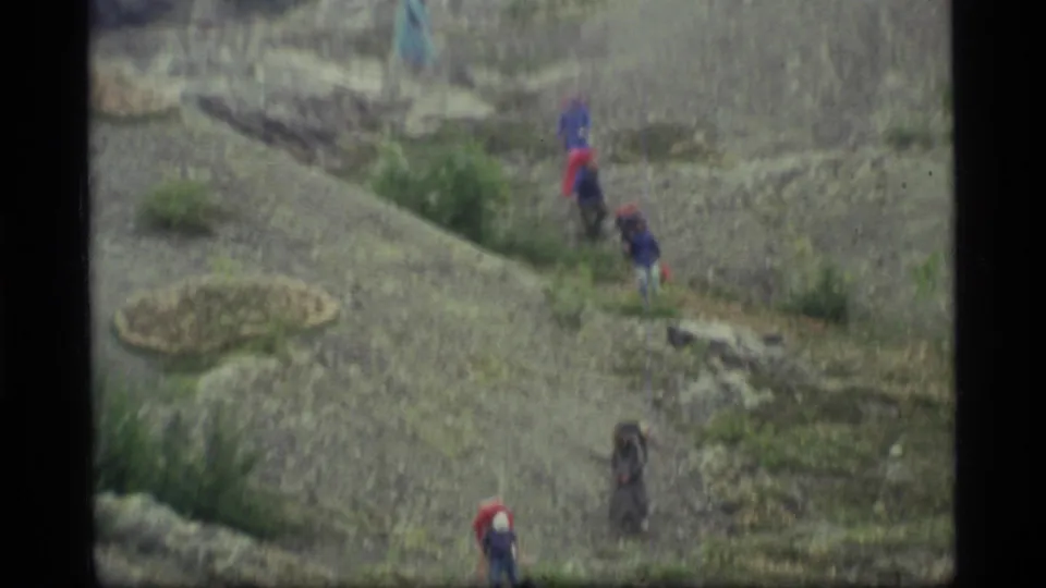 Distant hikers in colorful outdoor clothing move down a gray rocky hillside in Glacier Bay, Alaska.