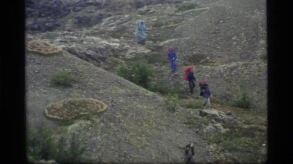 Home-movie view of several backpacked hikers crossing a rocky Glacier Bay slope in muted 8mm color.