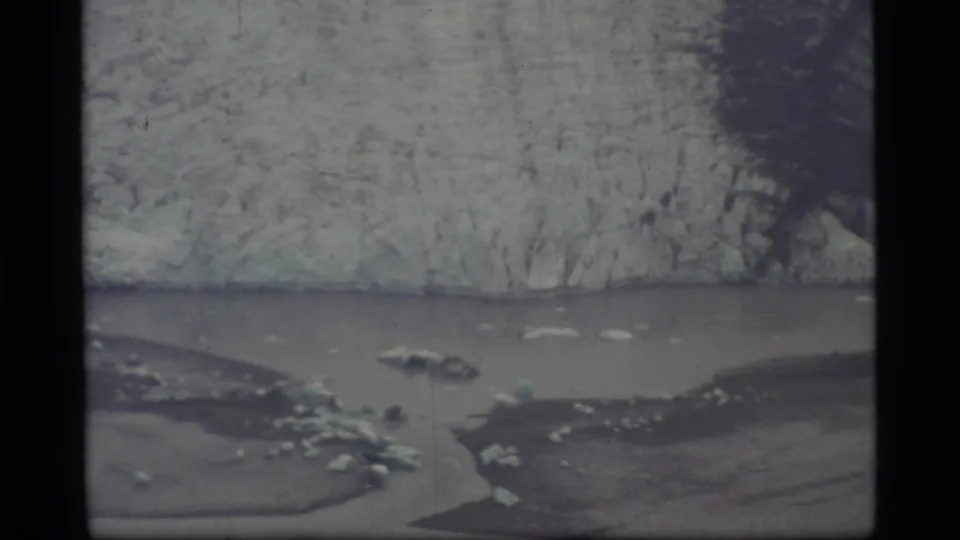 1977 Glacier Bay home-movie frame with textured glacier ice, calm water, dark landforms, and scattered ice floes.