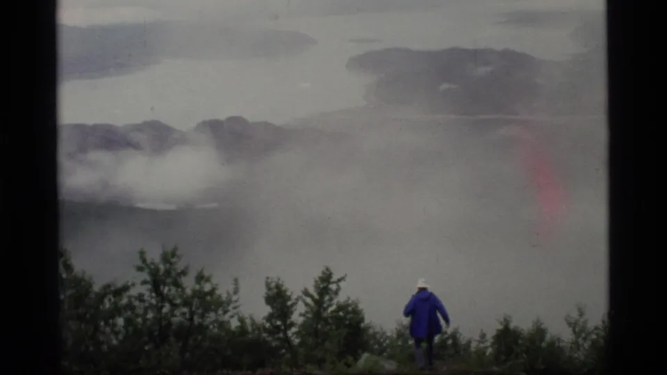 1977 Glacier Bay, Alaska 8mm frame showing a distant blue-coated hiker against mist, water, and dark mountain or island shapes.