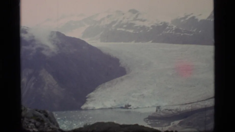 Wide 1977 Glacier Bay landscape frame showing a large glacier between mountain slopes, water below, and soft faded 8mm color.