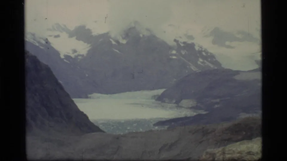 Glacier Bay, Alaska landscape with snow-covered peaks, pale glacial water or ice, and rugged slopes in vintage 8mm color.