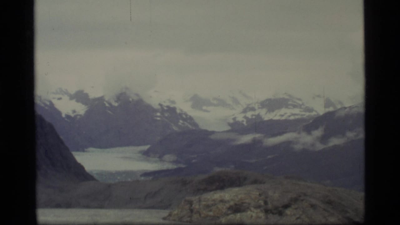 Wide view of snow-capped mountains and a distant icy valley under an overcast sky.