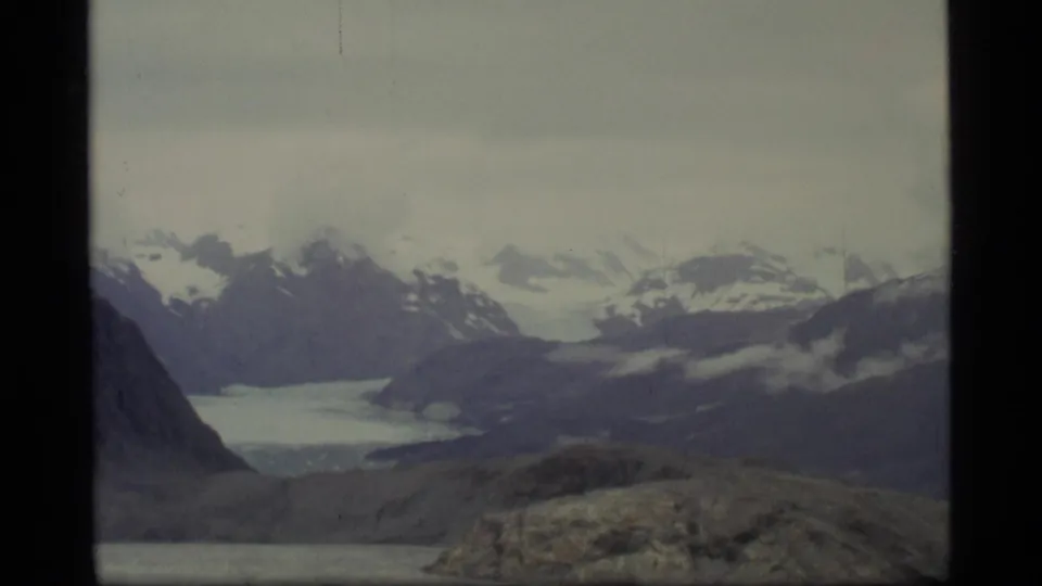 1977 Glacier Bay home-movie frame showing distant snow-capped mountains and a glacier-like valley from a high overlook.