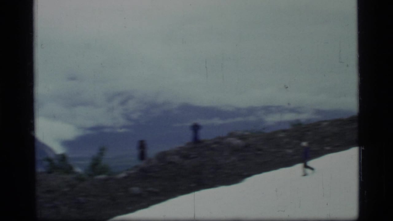 Hikers spread across a rocky ridge with snow below and mountains in the distance.