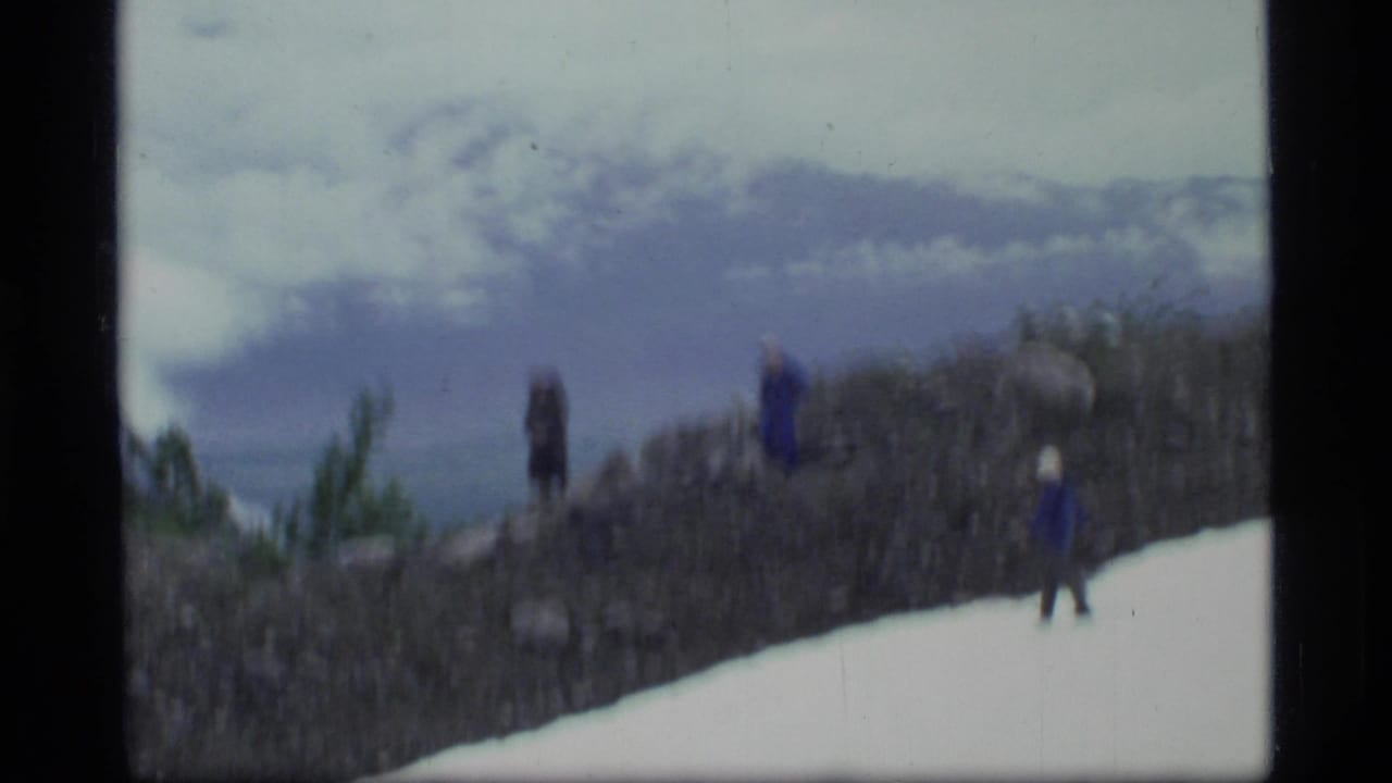 Hikers on a snowy rocky overlook with cloudy mountains beyond.