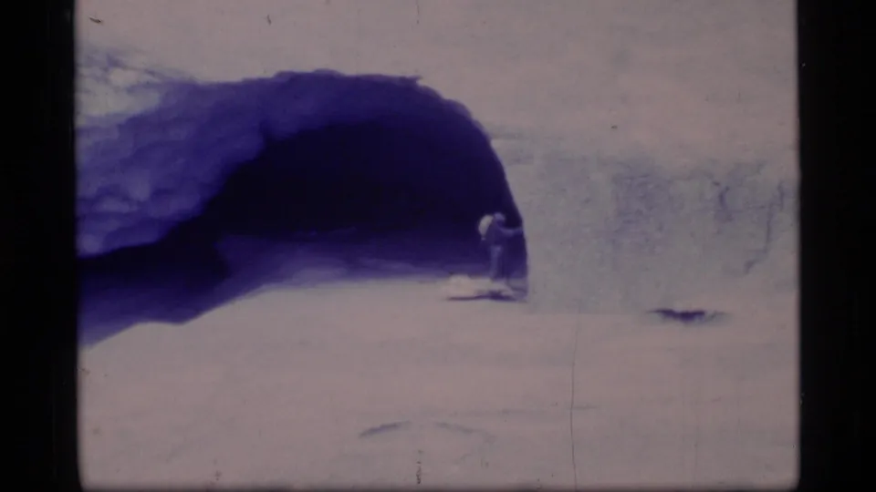 A distant person stands near a dark blue natural ice opening in the Glacier Bay snowfield, filmed in soft 8mm color.