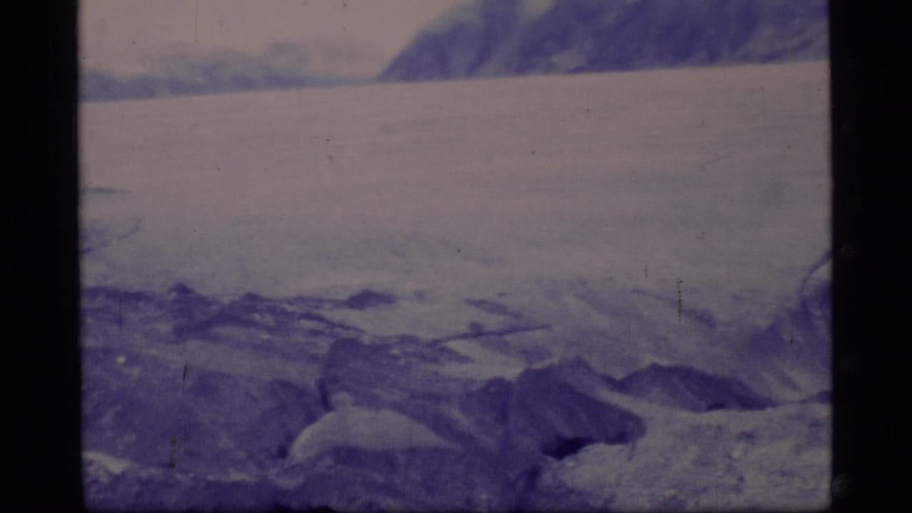 1977 Glacier Bay 8mm frame showing rough glacier ice, distant mountains, and a pale overcast sky.