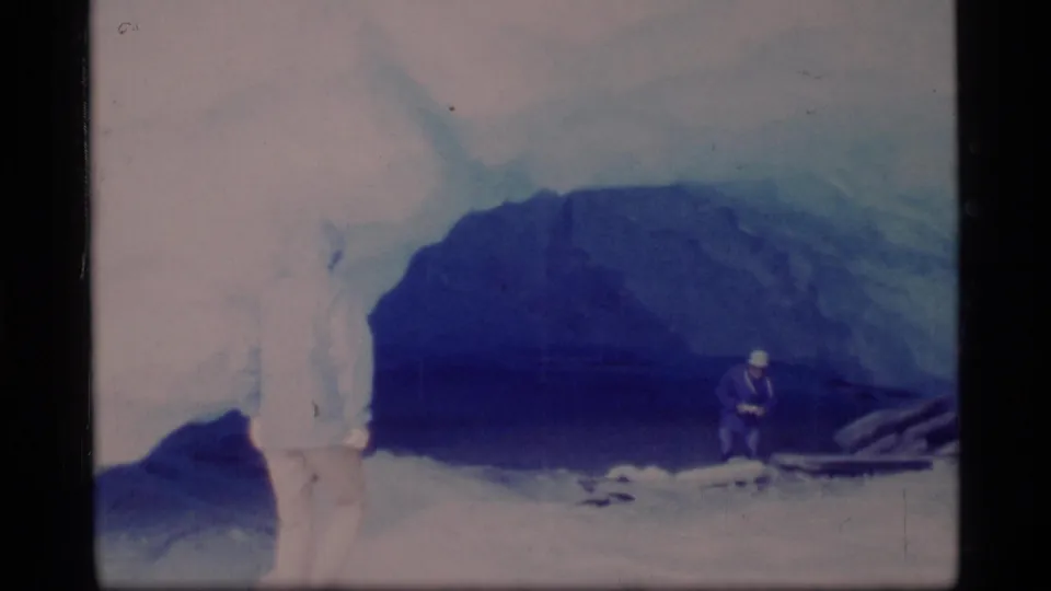 1977 Glacier Bay frame with people standing near a large blue ice cave during a glacier visit or expedition.