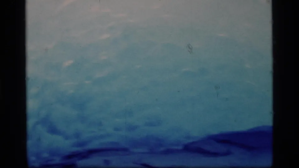 Glacier Bay landscape view in 1977 8mm footage, showing blue ice, distant ridges, and overcast sky.