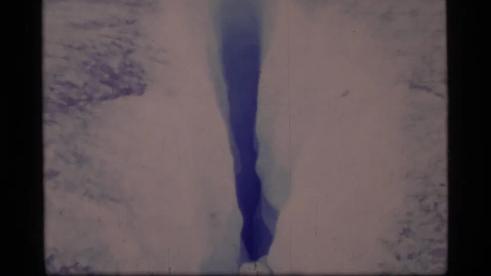A vertical view of a blue glacier crevasse in Glacier Bay, framed tightly within faded 8mm home-movie footage.