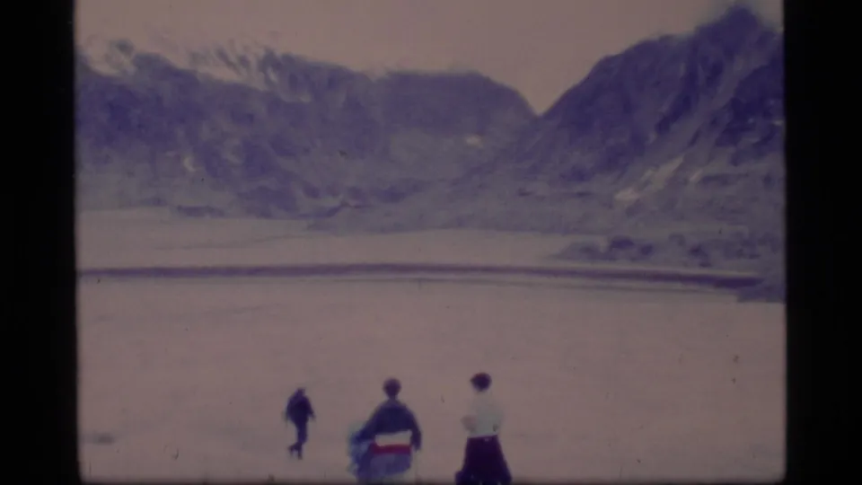 1977 Glacier Bay home-movie frame with three small figures on a broad pale surface below dark mountain slopes.