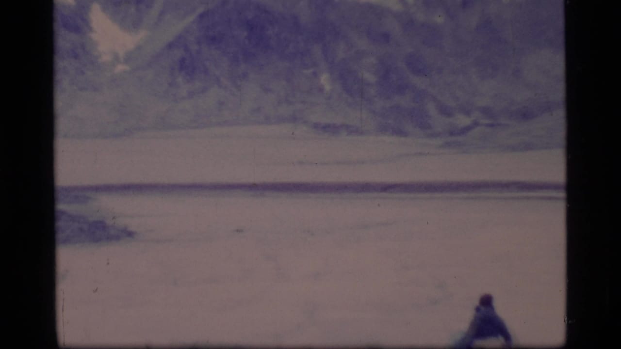 Distant hiker on a pale icy landscape with mountain slopes beyond.