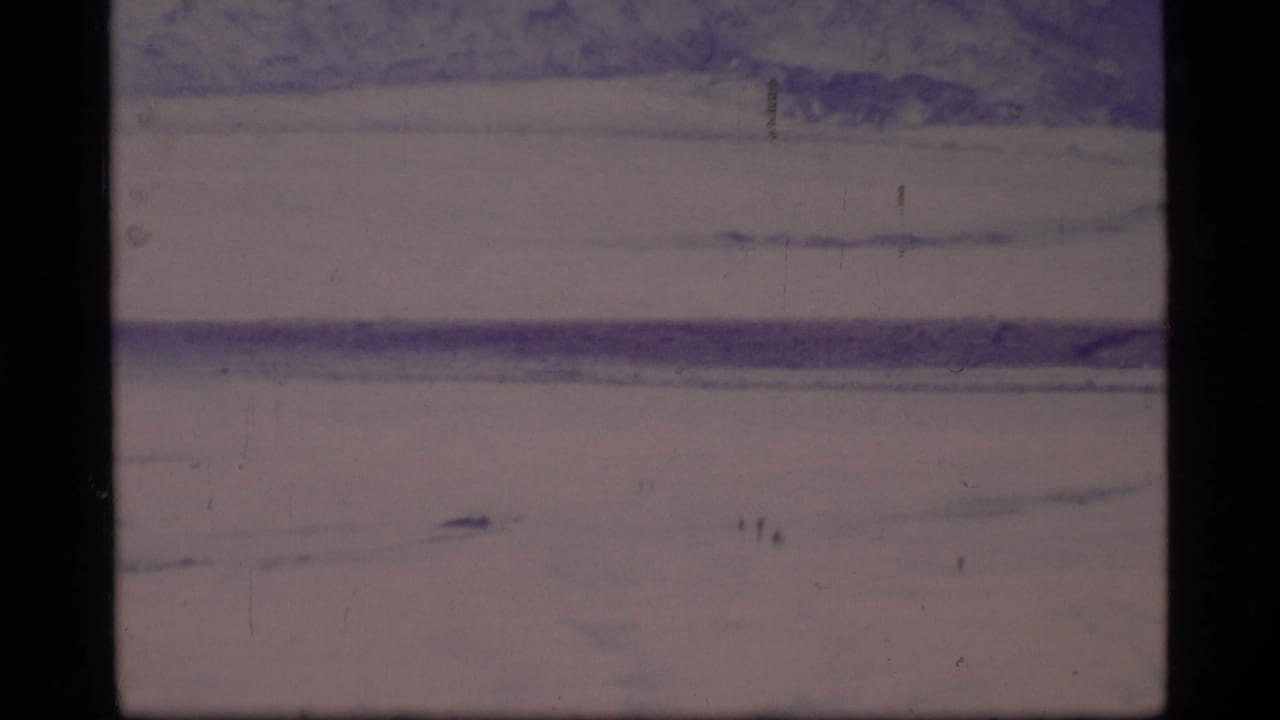 Wide icy plain with distant dark marks and mountains along the horizon.