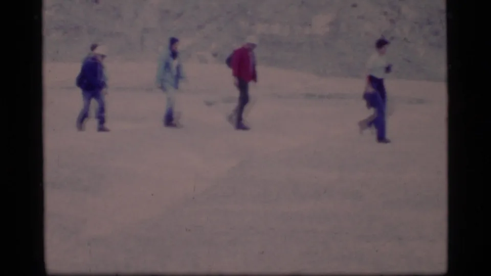 A 1977 Glacier Bay frame shows a small hiking group crossing open rocky ground, with backpacks, caps, and a red jacket visible.