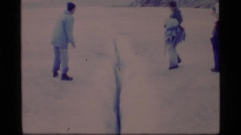 1977 Glacier Bay 8mm frame with bundled adults spaced apart on snow, framed by dark film borders.