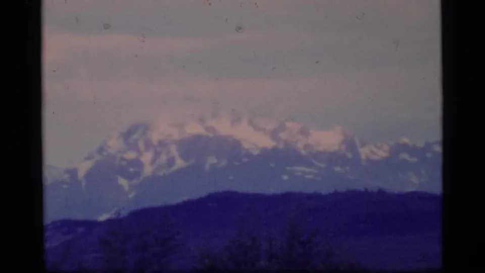 Glacier Bay mountain scenery with snowy peaks, a dark foreground ridge, and visible 8mm film borders.