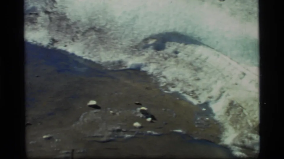 Glacier Bay meltwater appears beside a snow-covered bank, with small rocks visible on the dark wet surface.