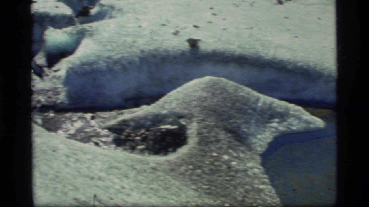 1977 Glacier Bay 8mm frame showing textured glacier ice, a melt channel, and dark sediment embedded in the snow surface.