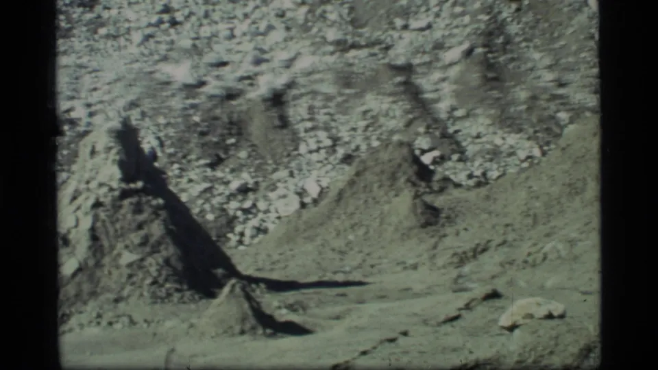 1977 Glacier Bay frame showing rough glacier ice, scattered debris, and a deep crevasse-like opening, with no people visible in this frame.