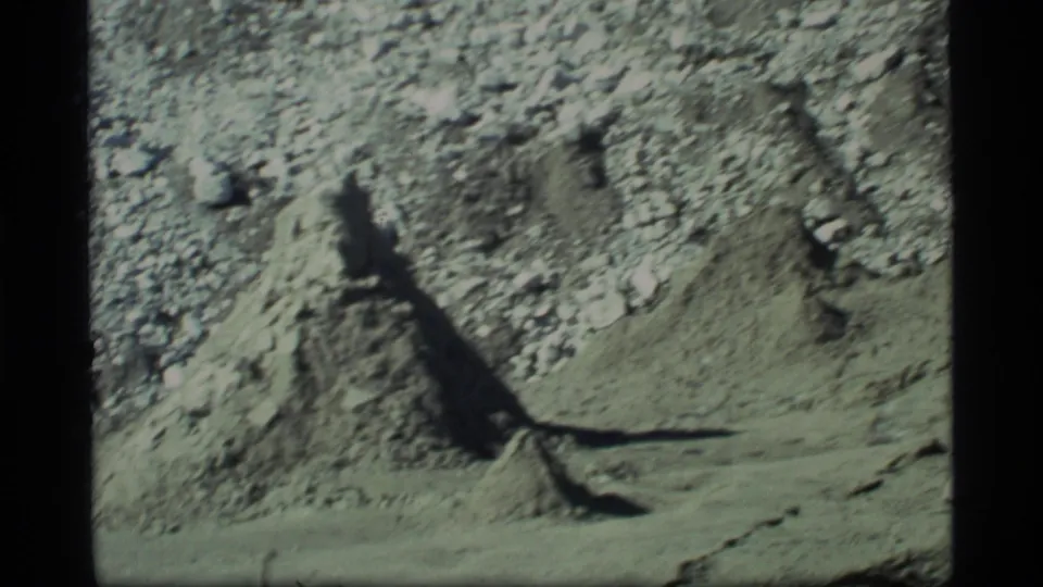 Glacier Bay, Alaska terrain in 1977, showing a rocky dirt bank and long shadow on pale barren ground.