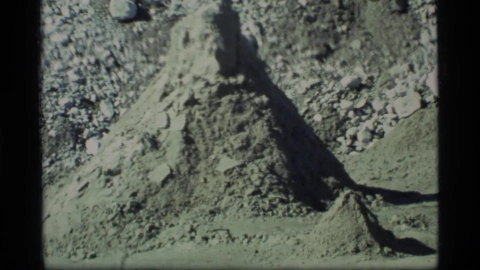 1977 Glacier Bay home-movie frame of a rough dirt mound, gravel slope, and dark shadow across barren terrain.