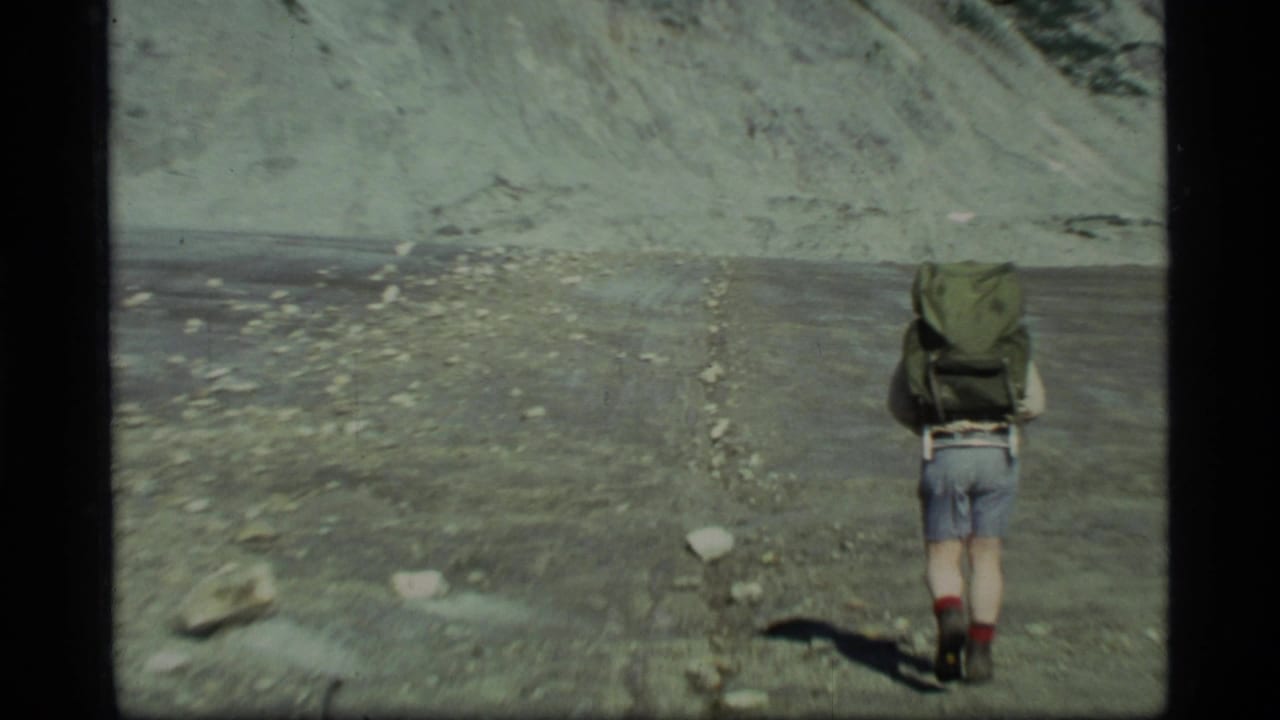 Backpacker walks away across rocky ground with a large pack.