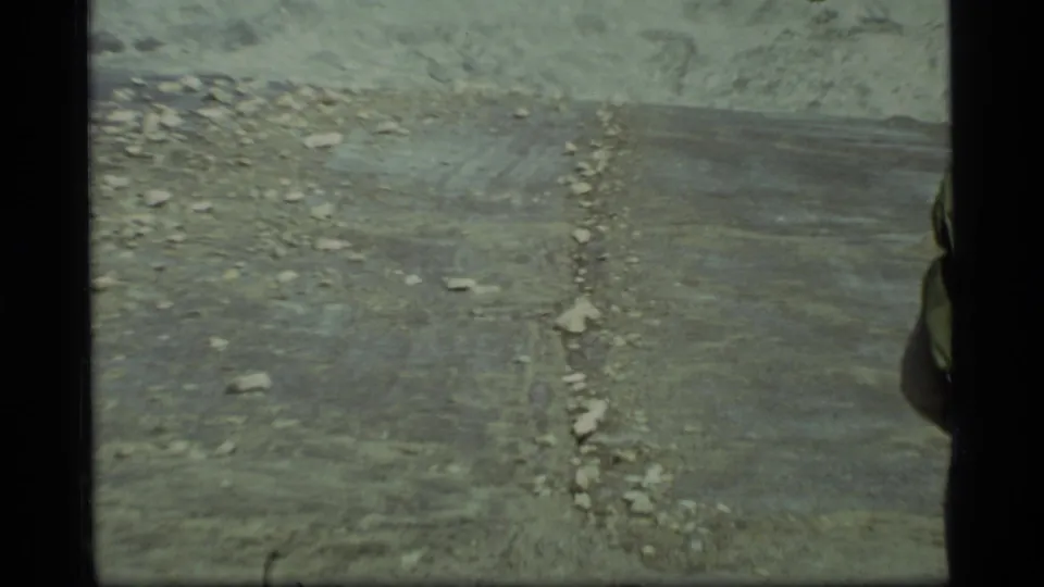 Dry rocky ground in Glacier Bay appears ahead, with the backpacker partly cropped at the right edge of the 8mm frame.