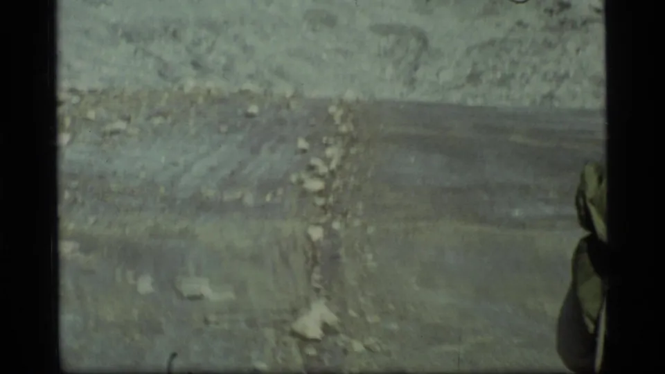 The handheld 8mm view softens as it follows rocky Glacier Bay ground, with the backpacker partially visible along the right edge.