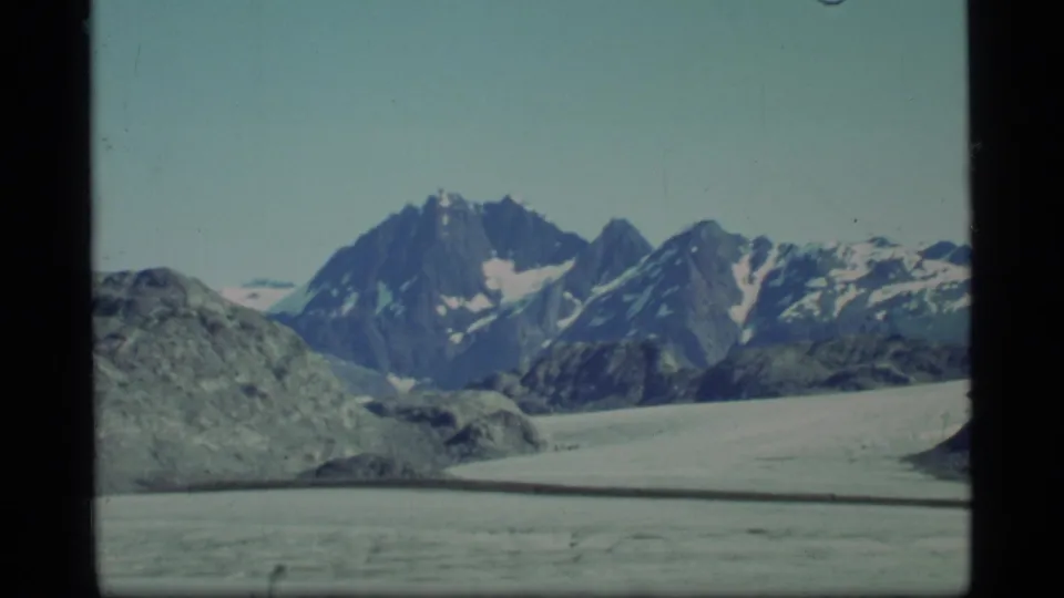 Glacier Bay mountain view on 8mm film, with jagged snow-marked peaks above a pale glacier or snowfield.