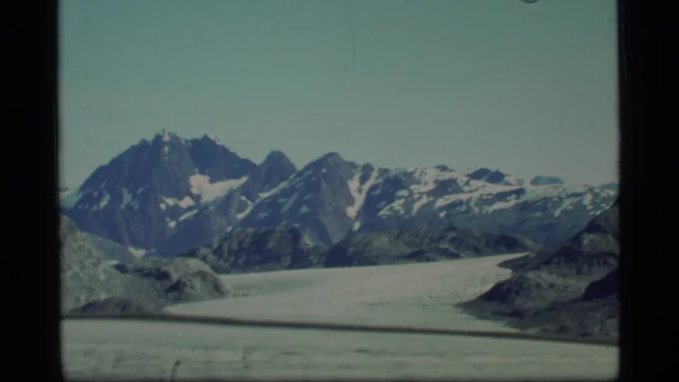 1977 Glacier Bay home-movie frame showing isolated peaks above a sweeping glacier with muted small-gauge film color.