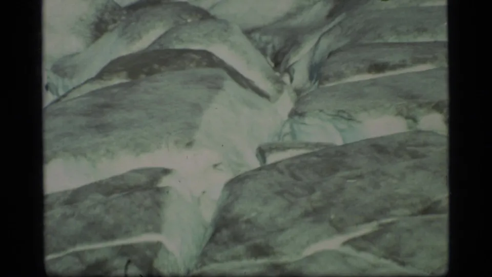 1977 Glacier Bay 8mm close-up of pale glacier ice shapes with dark crevasse lines and faded color.