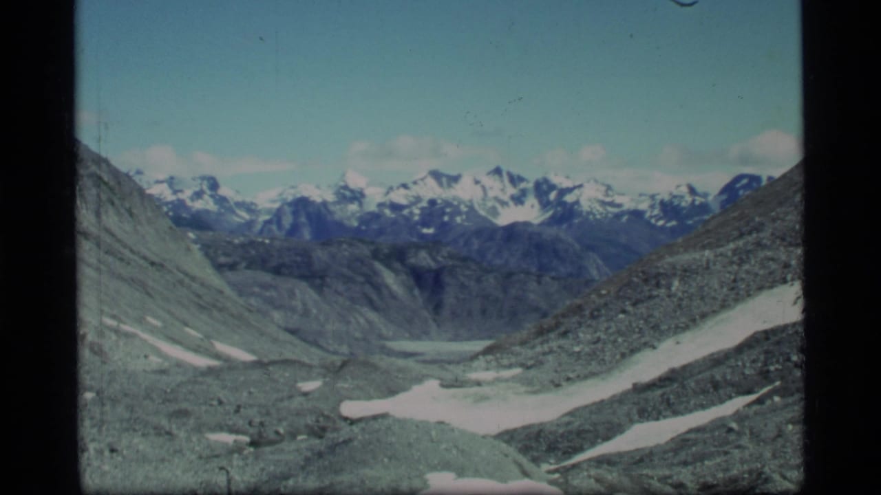 Wide view down a rocky valley toward distant snow-capped mountains.