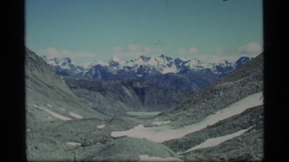 1977 Glacier Bay home-movie view of a glacial valley framed by gray slopes and snow-capped mountains.