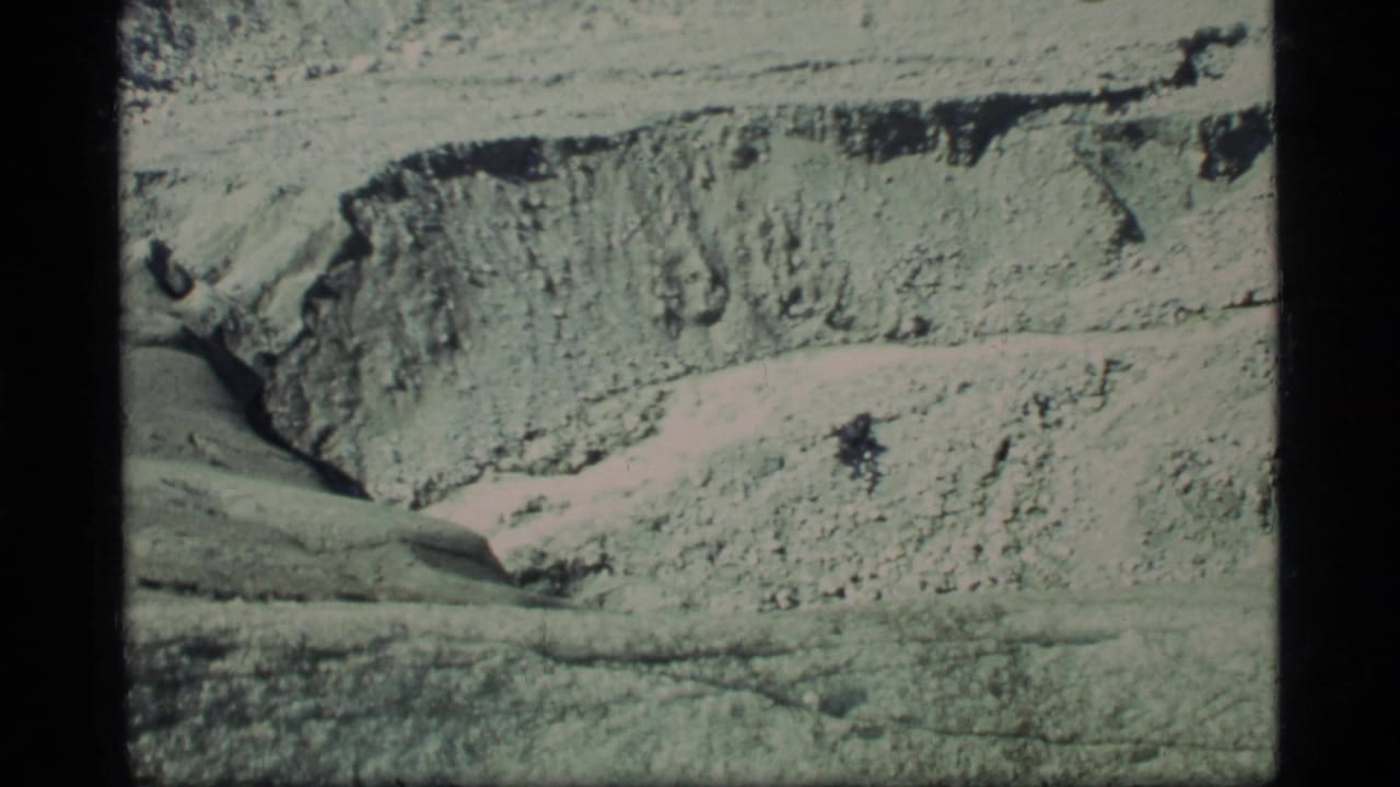 1977 Glacier Bay 8mm frame showing pale rugged terrain, layered rock texture, and a shadowed crevice line.