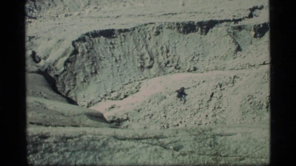 1977 Glacier Bay 8mm frame showing pale rugged terrain, layered rock texture, and a shadowed crevice line.