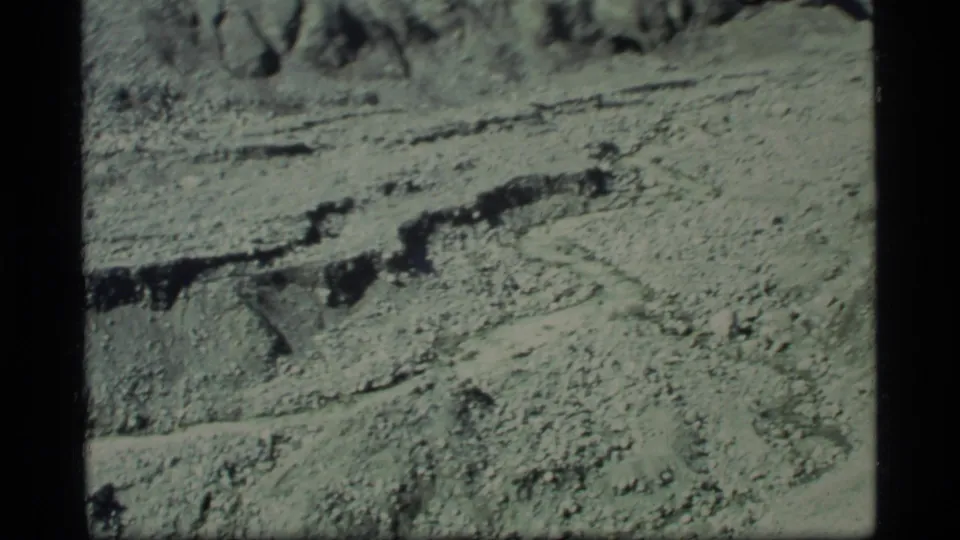 1977 Glacier Bay frame showing granular pale terrain, shadowed crevice lines, and layered geological forms.