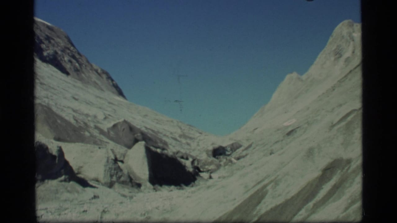 Glacier Bay home-movie frame showing jagged pale slopes, scattered rock, and a remote glacial valley in 1977 8mm footage.