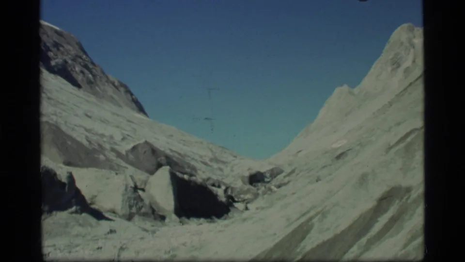 Glacier Bay home-movie frame showing jagged pale slopes, scattered rock, and a remote glacial valley in 1977 8mm footage.