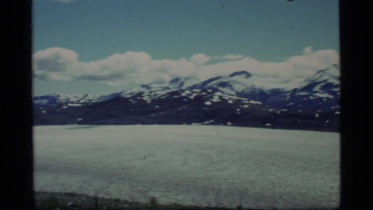 Wide glacier plain below snow-streaked mountains and clouds.