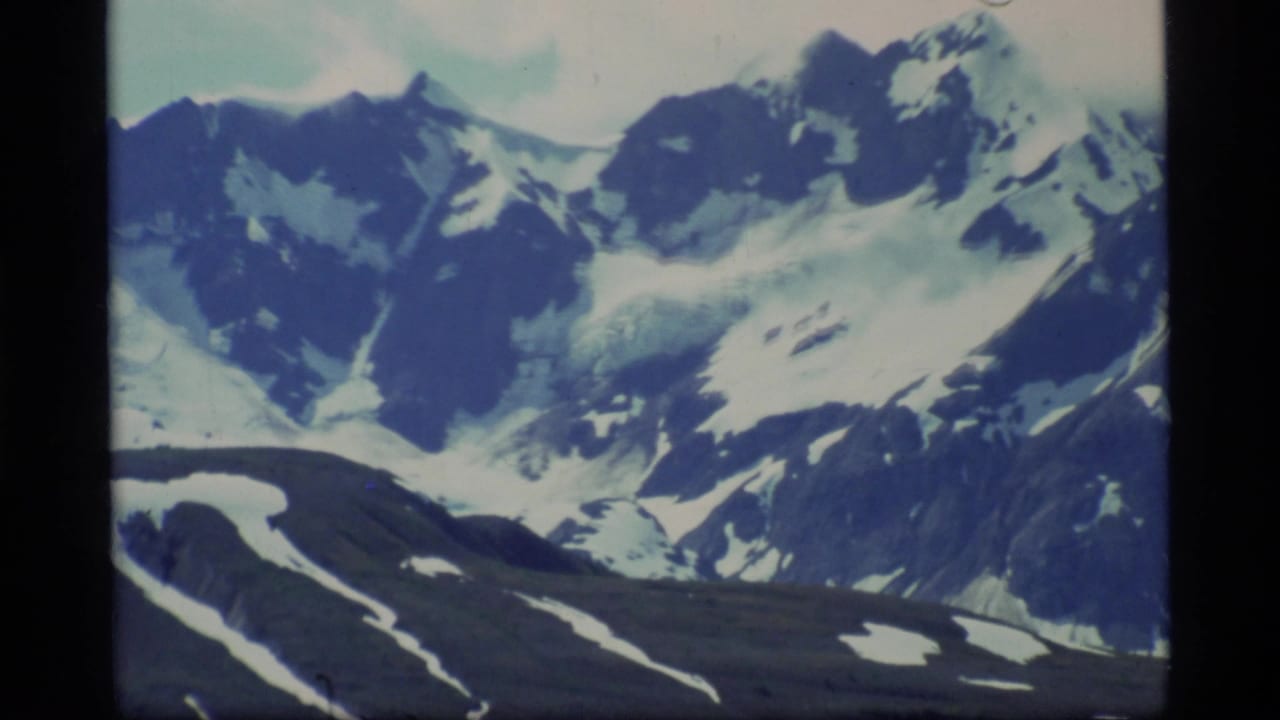 1977 8mm view of snow-capped mountains and glacier-like snowfields in Glacier Bay, Alaska, with soft blue-green film color.