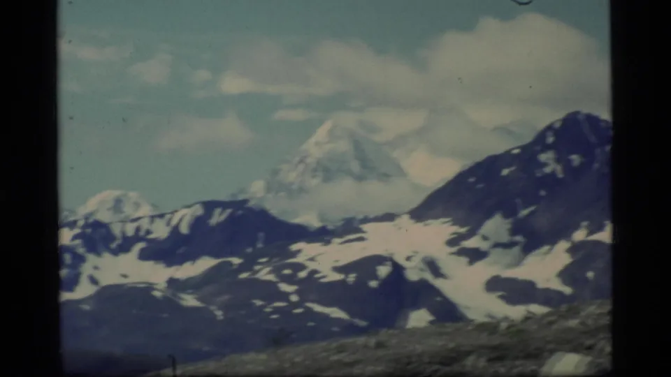 Glacier Bay mountain panorama on 8mm film, with snow patches, cloud cover, and a dark ridge at right.
