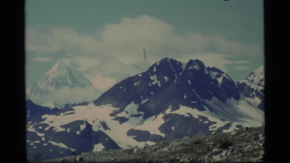1977 Glacier Bay view of snow-covered peaks partly softened by cloud, with a dark mountain slope in front.